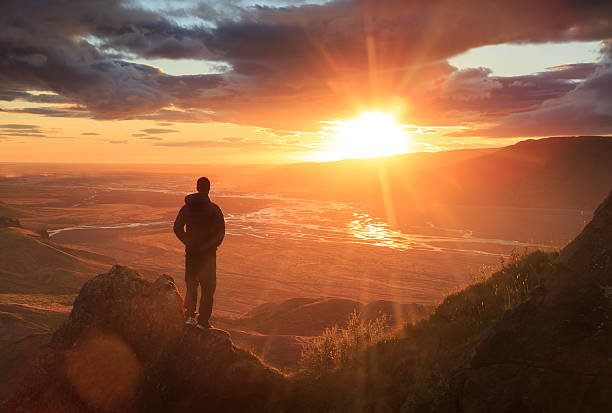 man standing on mountain looking at a sunset